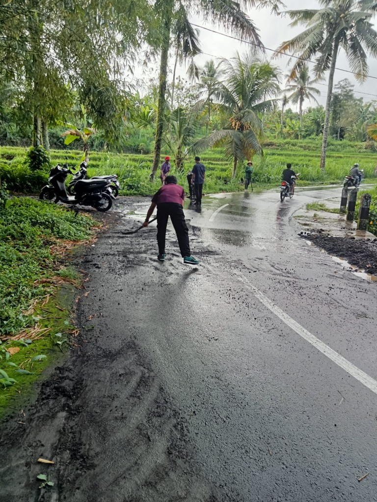 Rawan Kecelakaan, Babinsa Semarapura Kaja Gerak Cepat  Bersihkan Pasir Dan Koral Berserakan Di Jalan Raya, 